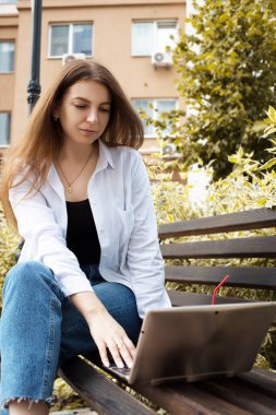 Genç ve güzel bir kadın parkta dizüstü bilgisayar için çalışıyor..