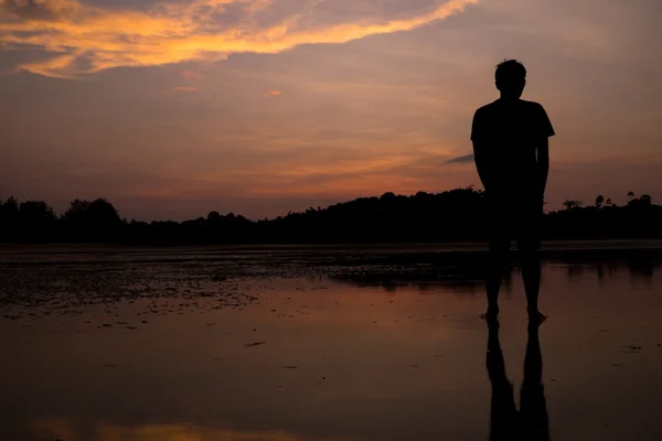 Homme sur la plage avec reflet dans l'eau au coucher du soleil . — Photo