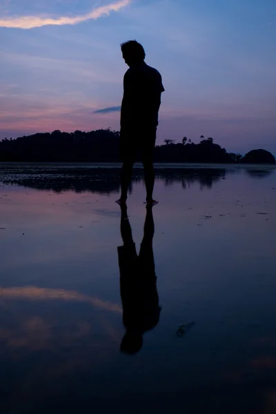 Homme sur la plage avec reflet dans l'eau au coucher du soleil . — Photo