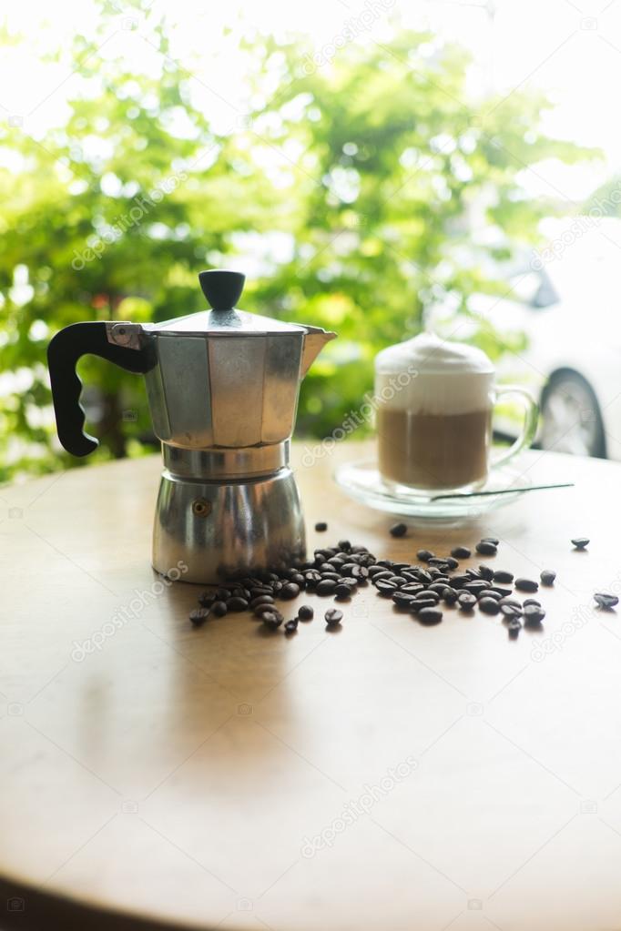 a moka pot and a cup of coffee with roasted coffee beans
