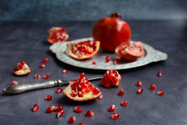 Koyu arkaplanda servis edilen gümüş bir tabakta olgun nar taneleri ve dilimleri. Yakın plan.