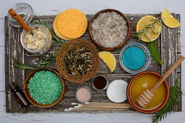 Arrangement of jars and bowls of cereals, scrubs, sea salt, essential oils, and honey on a brown wooden tray. Spa and bath concept. Top view