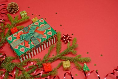 Kırmızı arka planda, metin ve tasarım için yeri olan bir Noel düzeni. Hediye kutusu, köknar dalları, çelenkler, dekoratif hediyeler ve yıldızlar..