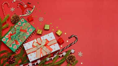 Hediye kutuları, Noel süslemeleri, köknar dalları, flama, kırmızı arka planda fotokopi alanı olan şeker kamışları. Pankart.