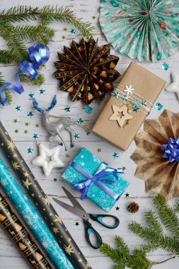 Noel dikey kompozisyonu. Mavi hediye kutuları, yıldızlar, ışıltılar, makas, tahta arka planda ambalaj kağıdı. Yukarıdan görüntüle