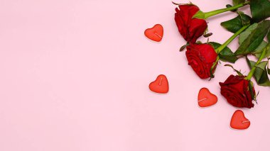 Kırmızı gül buketi ve pembe arka planda mumlar, üst manzara. Pankart