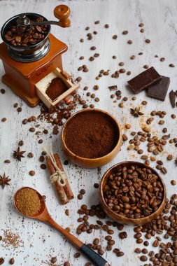 İki kâse kahve çekirdekli ve öğütülmüş kahve, kahve öğütücü, hafif ahşap zemin üzerinde tarçın çubukları. Üst Manzara. Dikey