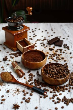 İki kâse kahve çekirdekli ve öğütülmüş kahve, bir kahve değirmeni, hafif ahşap arka planda tarçın çubukları. Yukarıdan bak. Dikey