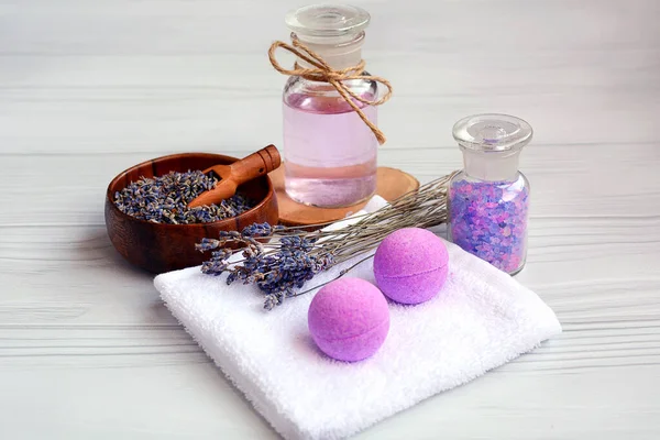 Banyo ve spa için kompozisyon. Renkli deniz tuzu, lavanta, yağ ve hafif ahşap arka planda bir havlu.