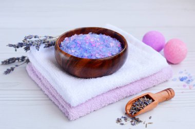 Bir yığın havlunun üzerindeki ahşap bir kasede renkli deniz tuzu. Sauna ve spa konsepti.