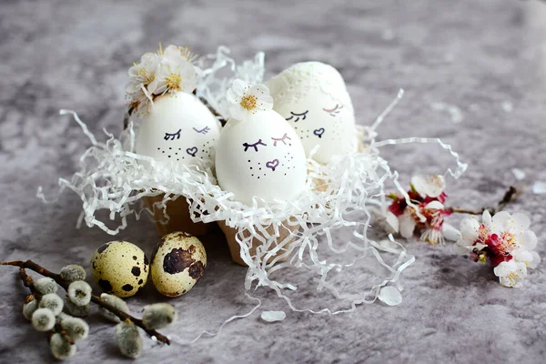 White eggs with faces painted on them in a decorative nest with pussy willow branches and cherry blossoms. Easter holiday