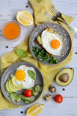 İki kişilik kahvaltı. Tabaklarda, domateslerde, avokadoda iştah açıcı yumurtalar ve hafif ahşap arka planda servis edilen sarı bir peçetede kızarmış ekmek. Dikey
