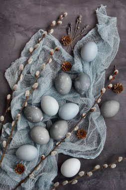 Vertical layout for the Easter holiday. Gray, blue, marbled eggs and pussy willow branches on a dark gray background. View from above.