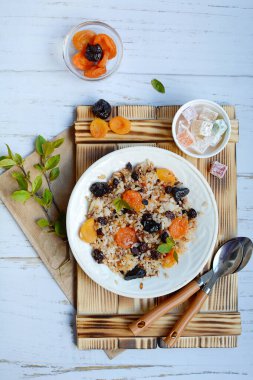 Kurumuş meyveli pirinç lapası, şekerli meyve ve hafif arka planda kaşıklar olan tahta tepsinin dikey görüntüsü. Yukarıdan bak. Lezzetli ve sağlıklı kahvaltı konsepti