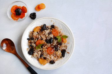 Beyaz tabakta kurutulmuş kayısı, kuru erik ve kuru üzümlü pirinç lapası. Sağlıklı kahvaltı kavramı