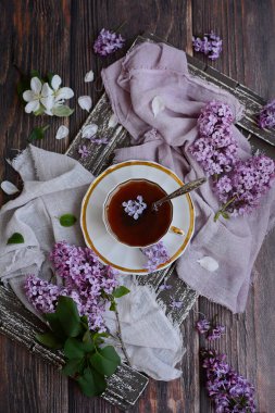 Dikey kompozisyon. Kahverengi tepside etrafında leylak çiçekleri olan beyaz fincanlar. Yukarıdan görüntüle