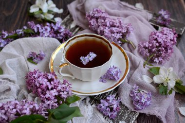 Etrafında leylak çiçekleri ve elma ağaçları olan kahverengi tepside çay ile beyaz bir porselen bardağın yakın plan çekimi..