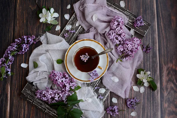 Kahverengi tepside çay ve leylak çiçekleri olan beyaz bardakların üst görüntüsü. Bahar Çay Konsepti