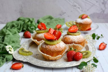 Açık gri ahşap arka planda çilekli ve kivili ev yapımı tatlı kekler, seçici odak. Lezzetli ve sağlıklı kahvaltı konsepti.