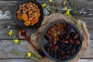 Kuru erik, hurma, kuru üzüm, kayısılar ve gri ahşap arka plandaki metal kaselerde badem. Yukarıdan görüntüle