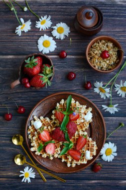 Koyu ahşap arka planda çilekli waffle ve papatya çiçeği. Üst görünüm, dikey görüntü.