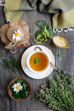 Dikey kompozisyon. Beyaz fincanda bitki çayı, nane, ıhlamur, kekik ve bal. Yukarıdan görüntüle