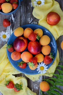 Vertical composition. Ripe, juicy peaches, apricots and strawberries on a gray wooden background. Close-up
