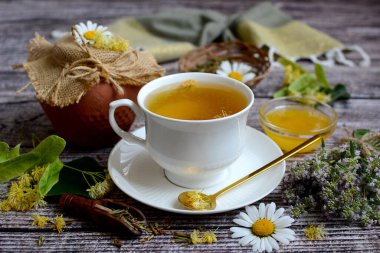 Composition of medicinal herbs. white cup with herbal tea, linden flowers, thyme, honey and chamomile flowers on a wooden background. Closeup