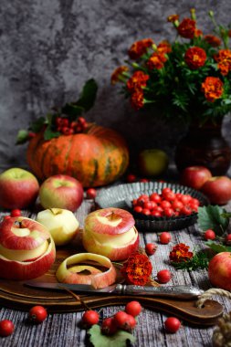 Sonbahar hala koyu renklerde. Sulu kırmızı elmalar, dikenli meyveler, gri arka planda balkabağı. Dikey