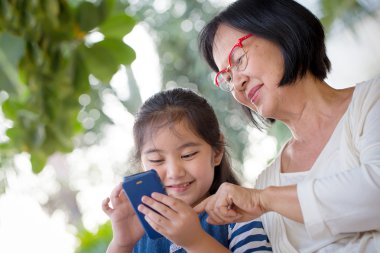 Little Asian girl using mobile phone with her grandmother clipart