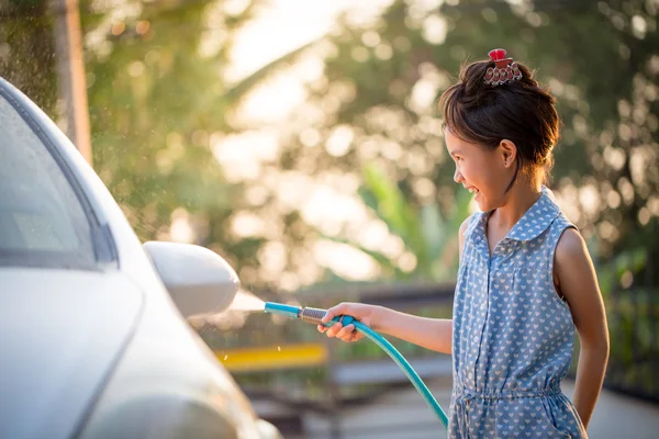 Happy Asian girl washing car on water splashing and sunlight at home