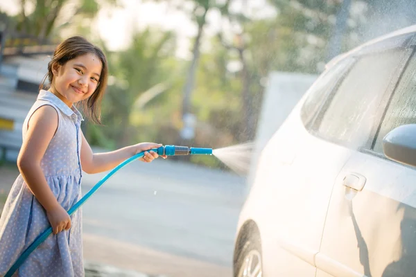 Happy Asian girl washing car on water splashing and sunlight at home