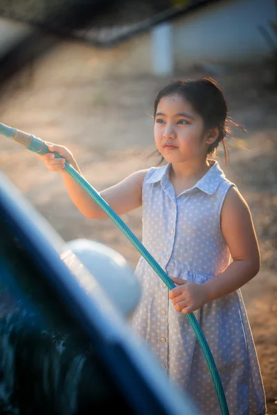 Feliz chica asiática lavando coche en el agua salpicaduras y la luz del sol en casa — Foto de Stock