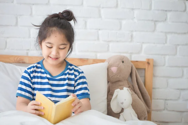 Happy Asian girl reading story book on the bed