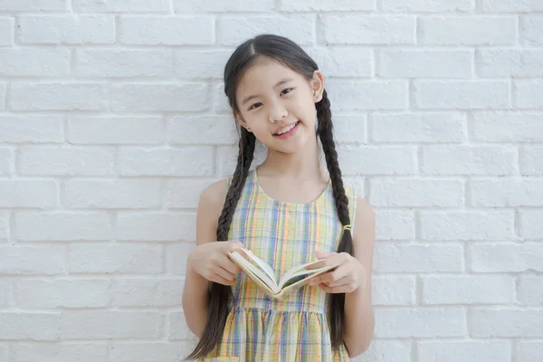 Menina asiática lendo livro história na parede de tijolo branco — Fotografia de Stock