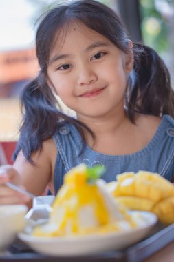 Happy Asian child enjoy eating with mango ice-cream clipart