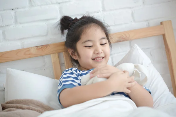 Liten asiatisk flicka kramar dockan på sängen — Stockfoto