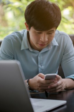 Kafede dizüstü bilgisayar ve akıllı telefon kullanan genç Asyalı adam