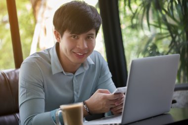 Kafede dizüstü bilgisayar ve akıllı telefon kullanan genç Asyalı adam