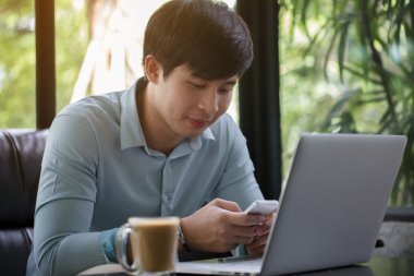 Kafede dizüstü bilgisayar ve akıllı telefon kullanan genç Asyalı adam