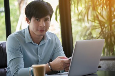 Kafede dizüstü bilgisayar ve akıllı telefon kullanan genç Asyalı adam