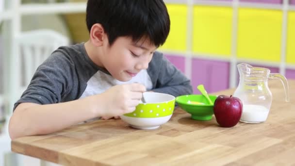 Маленький азіатський хлопчик їсть зернові з молоком з посмішкою обличчя — стокове відео