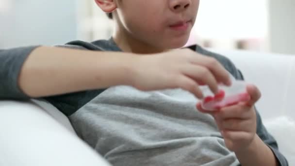 Shot de asiático lindo chico comer un piruleta con divertido cara expresiones . — Vídeo de stock