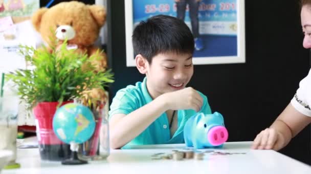 Ásia mãe ajudando filho para economizar dinheiro no porquinho banco — Vídeo de Stock