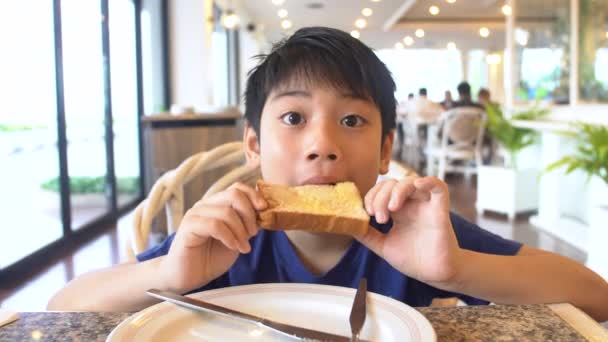 Asiático pré-adolescentes menino come pão sentado na mesa, 4K — Vídeo de Stock