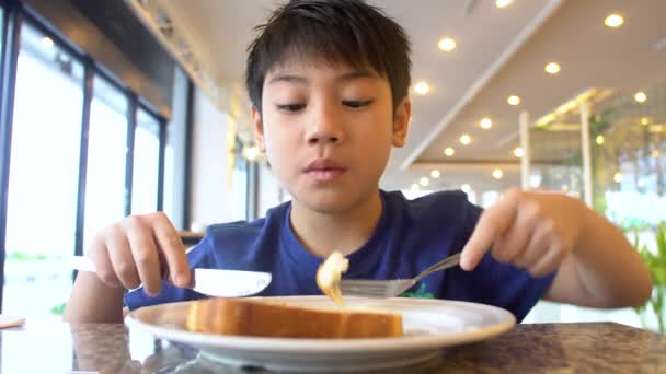 Asiático pré-adolescentes menino come pão sentado na mesa, 4K — Vídeo de Stock