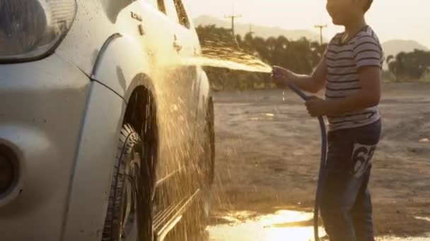 Happy asiatiska kid tvätta bilen med vatten spray.4k skjuta med solnedgång och flare skjuta av Sony A6300 — Stockvideo