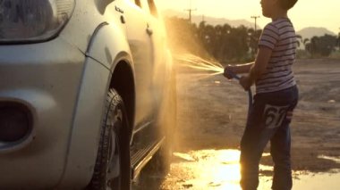 Mutlu Asyalı çocuk çamaşır araba su spreyi ile. Günbatımı ve flare, 120 Fps tarafından Sony A6300 ile yavaş çekim