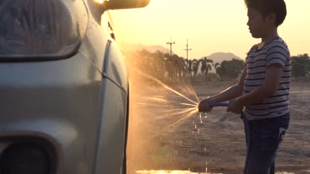 Gelukkig Aziatische jongen wassen auto met verneveld water. Slow motion shoot met zonsondergang en flare, 120 Fps door Sony A6300 — Stockvideo