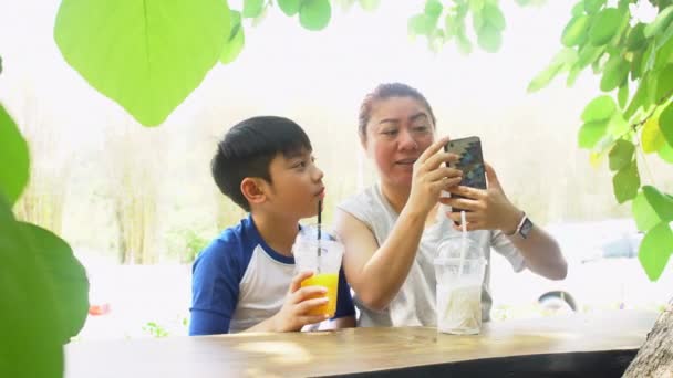 Madre e hijo asiáticos con teléfono inteligente en el jardín. 4K — Vídeo de stock